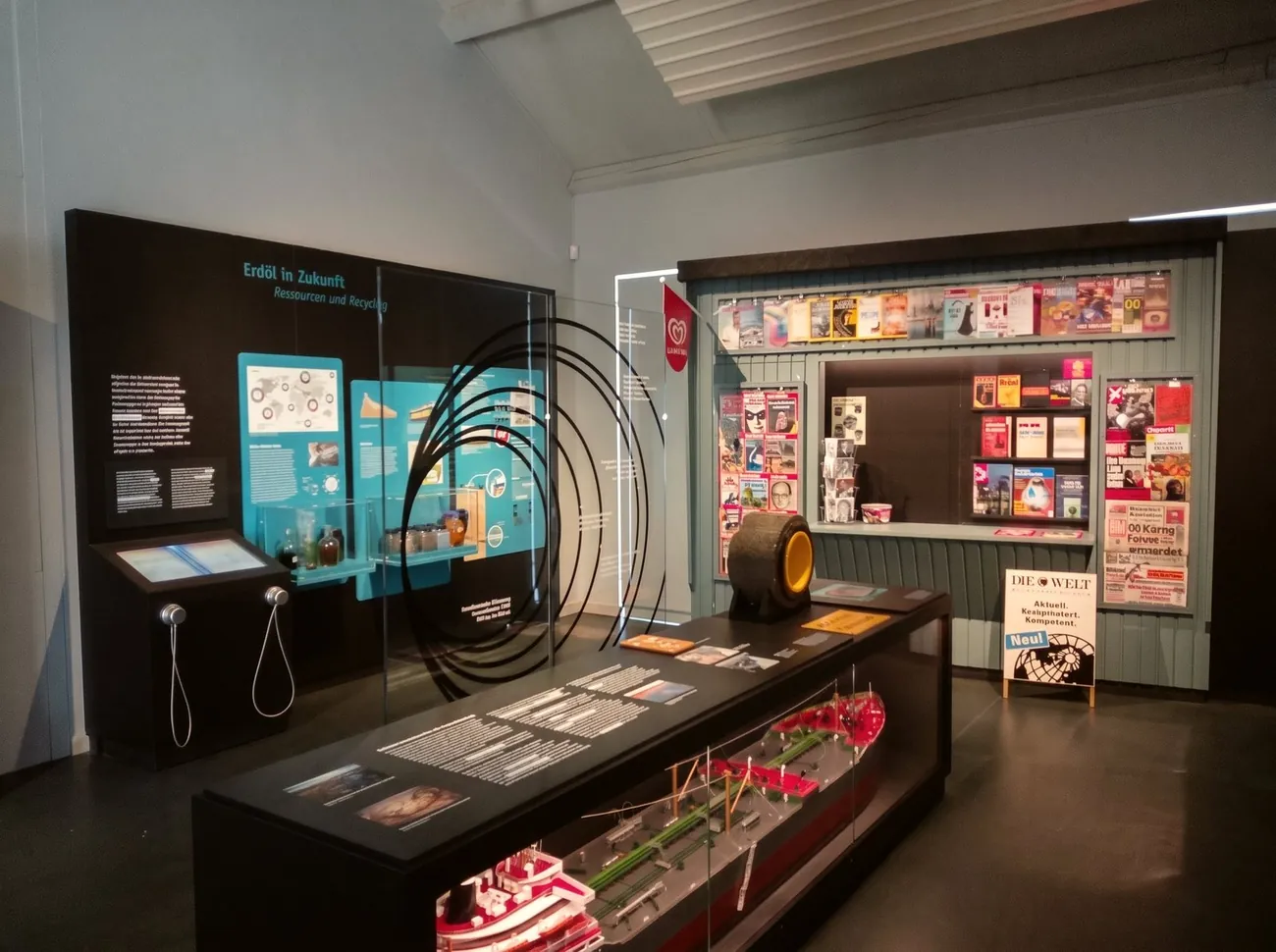Ausstellungsraum im Deutschen Erdölmuseum mit Vitrinen, Medienstationen und einer Wand voller historischer Werbeschilder